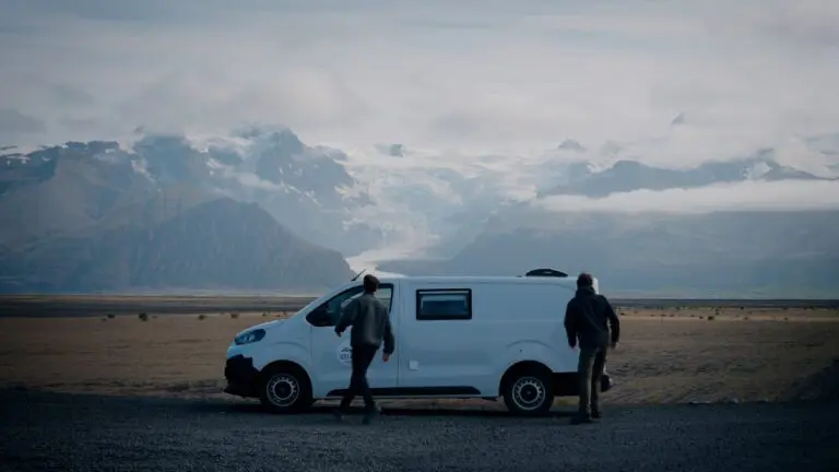 two people with a camper van in front of a glacier mountain range