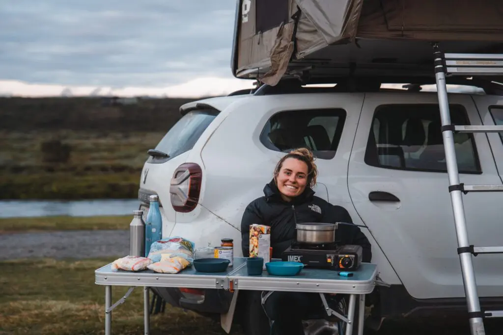 woman cooking outdoors next to car with rooftop tent in Iceland