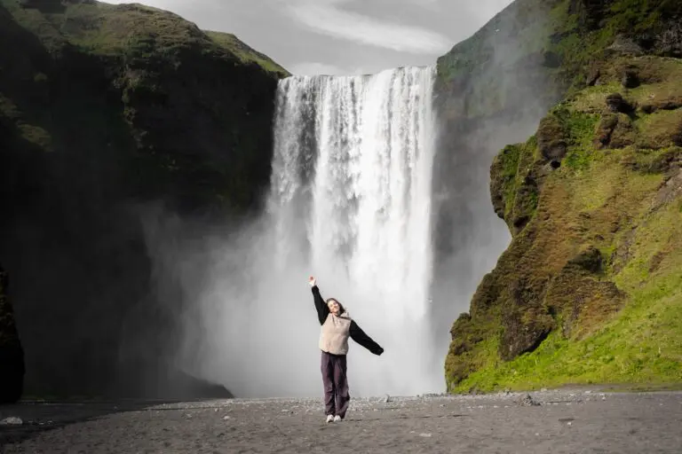 person jumping with arms raised in front of Skogafoss waterfall Iceland