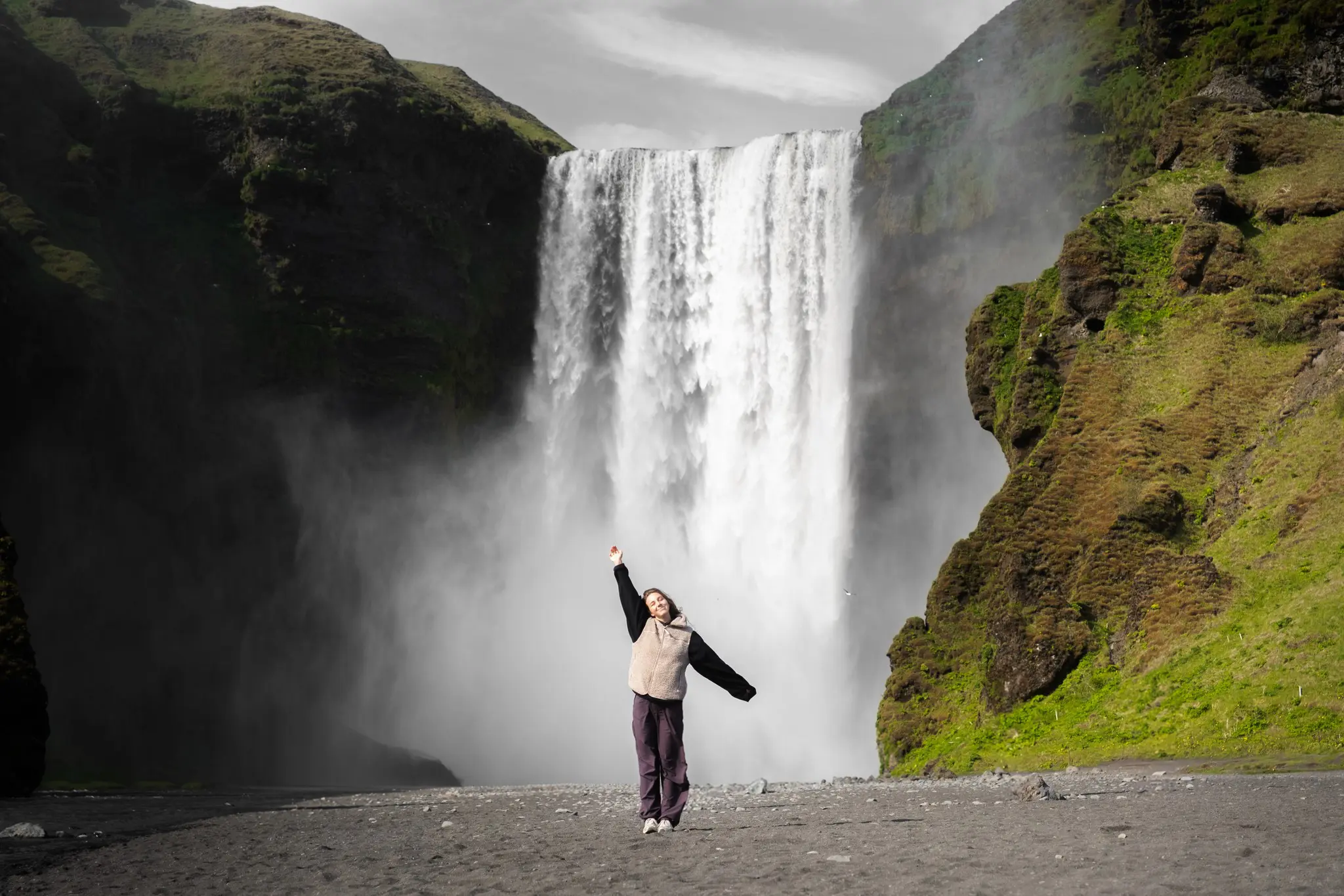 person jumping with arms raised in front of Skogafoss waterfall Iceland