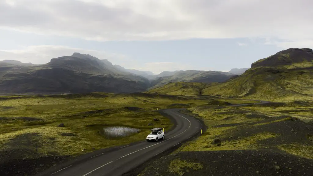 white camper van driving on a winding road through a green valley