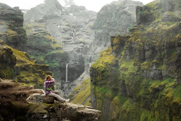 hiker sitting on cliff edge overlooking waterfall in Iceland