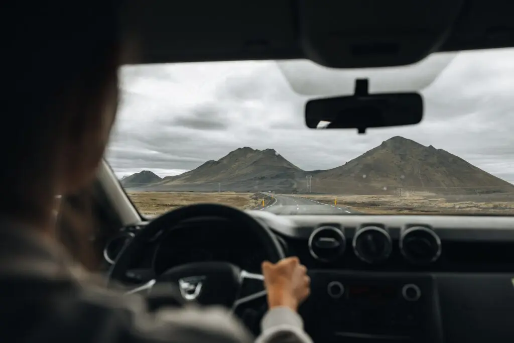 driving through icelandic landscape with mountains under cloudy sky