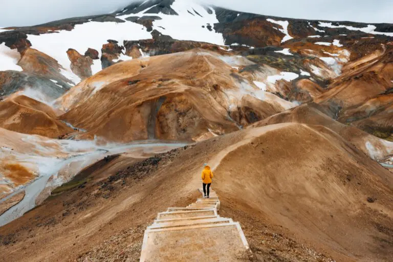 person in yellow jacket hiking on stairs in geothermal landscape