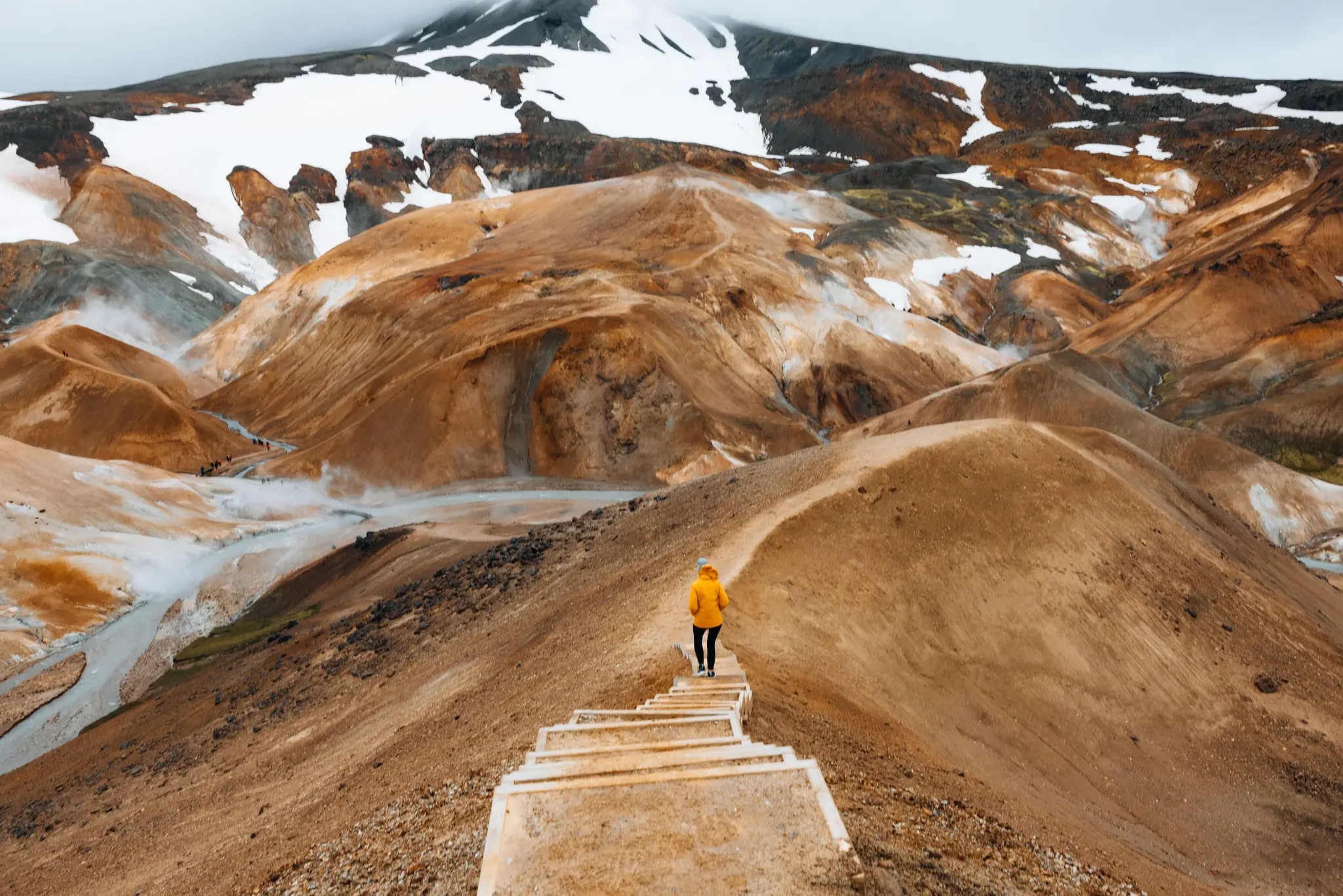 person in yellow jacket hiking on stairs in geothermal landscape