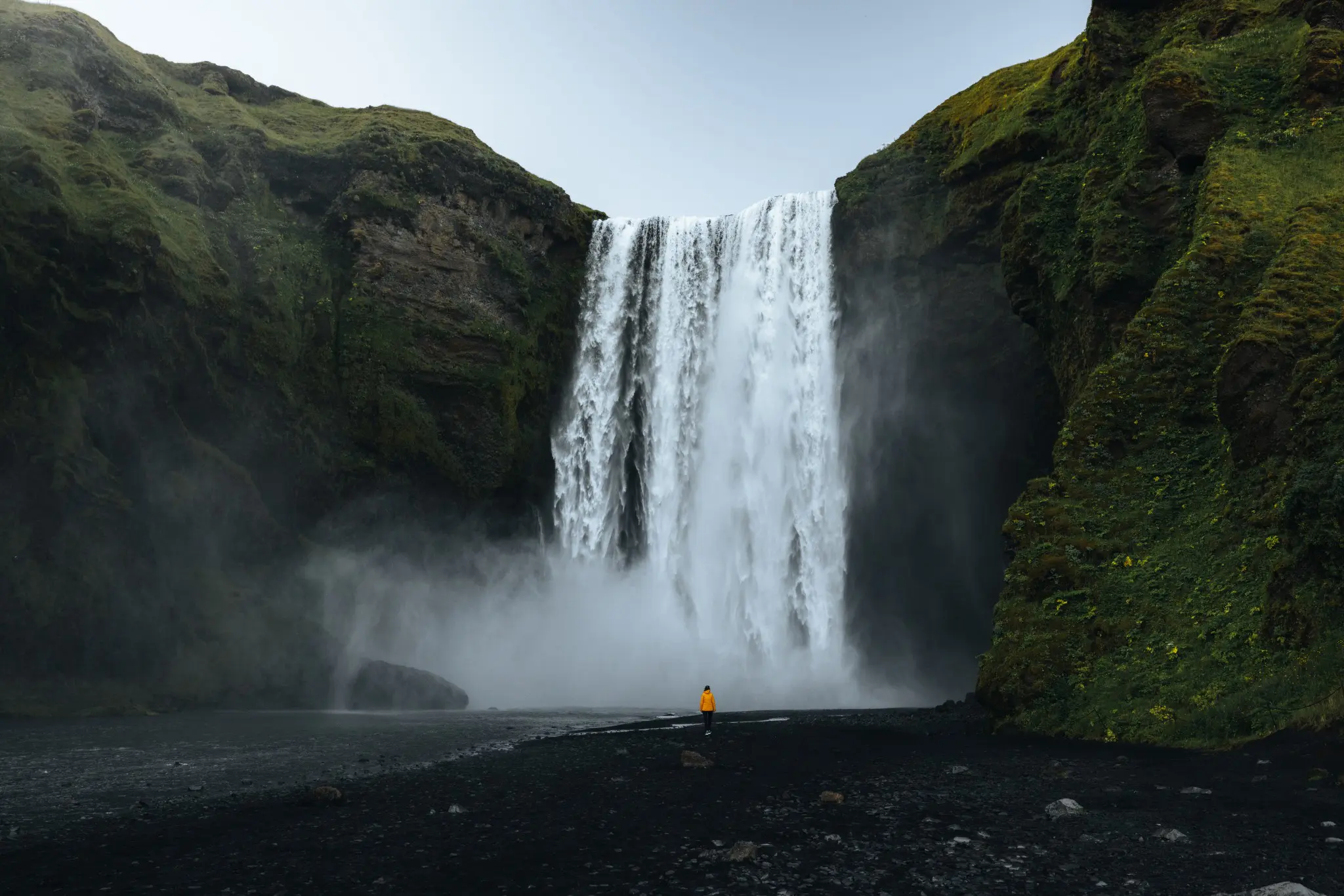 person in yellow jacket at Skogafoss waterfall in Iceland