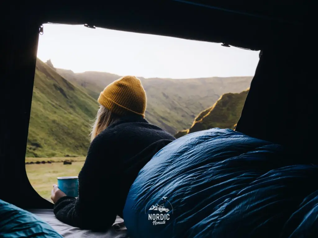 person in sleeping bag looking out of tent at mountains
