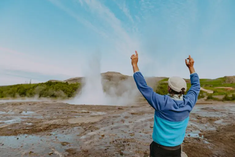 person with arms raised watching a geyser erupt in Iceland