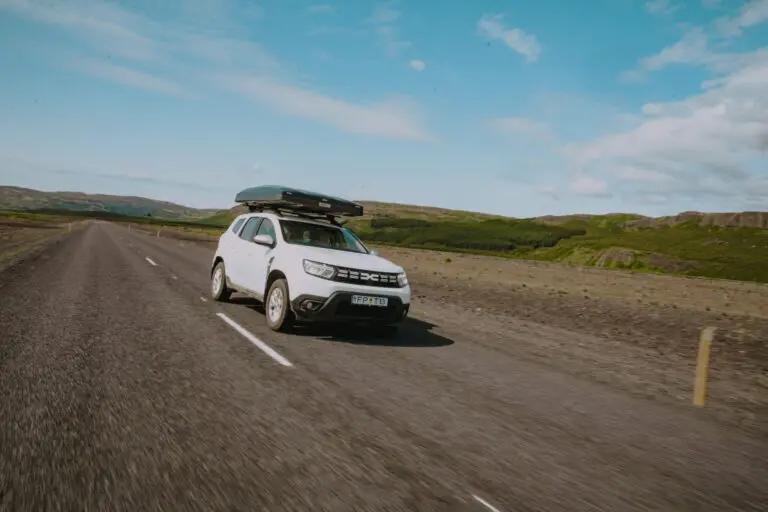 white car with rooftop tent driving on a road in Iceland