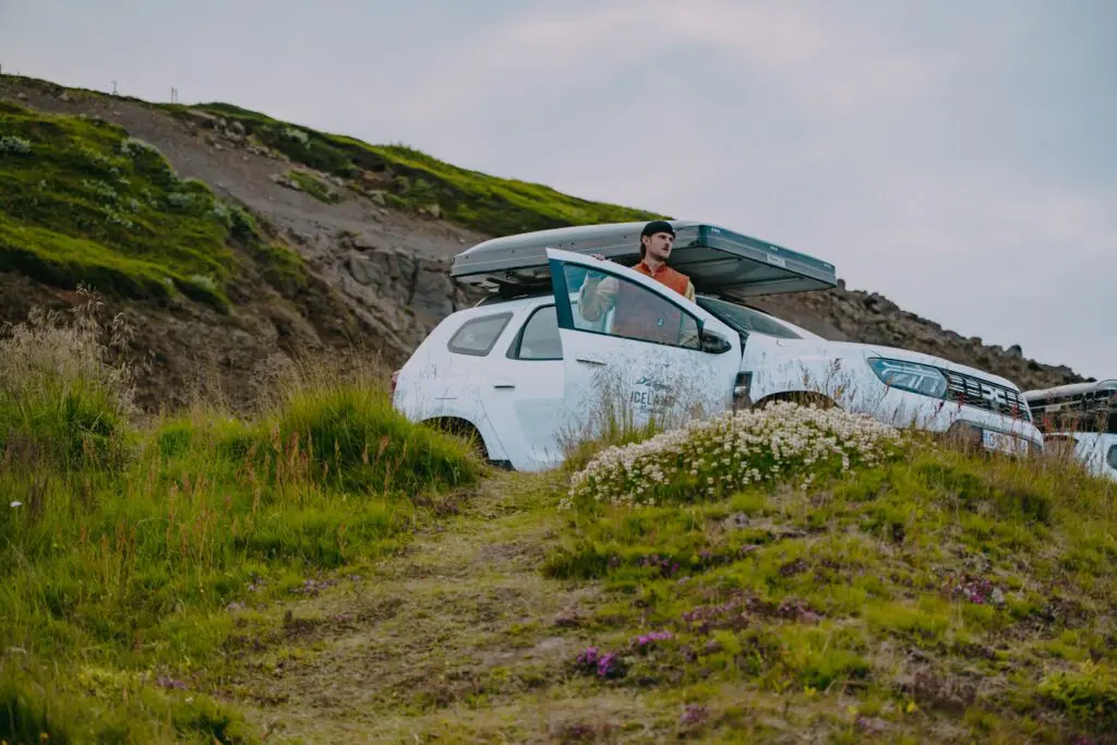 man standing by a white car with a rooftop tent in a green landscape