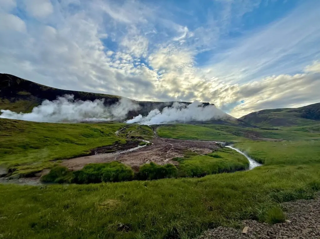 geothermal landscape with steam vents and green hills under cloudy sky