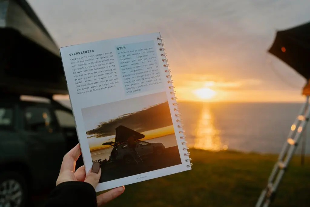 hand holding travel guide with campervan at sunset in Iceland