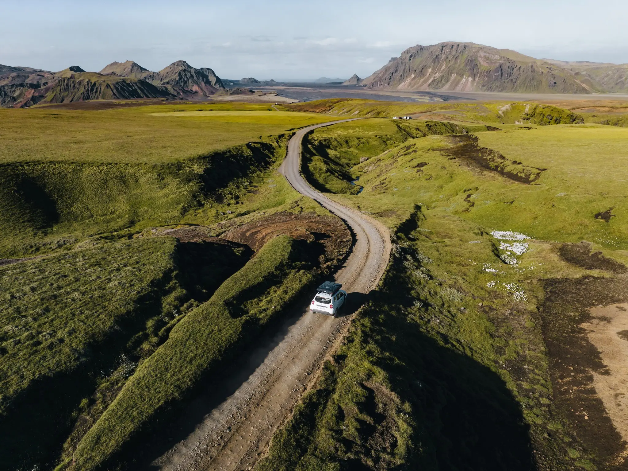 white car driving on winding dirt road in green Icelandic landscape