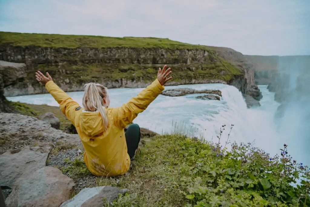 person in yellow jacket with arms raised at Gullfoss waterfall
