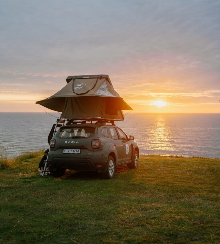 car with rooftop tent overlooking ocean at sunset