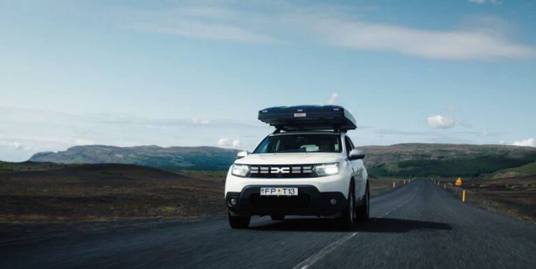 white Dacia Duster with rooftop tent driving on a road in Iceland
